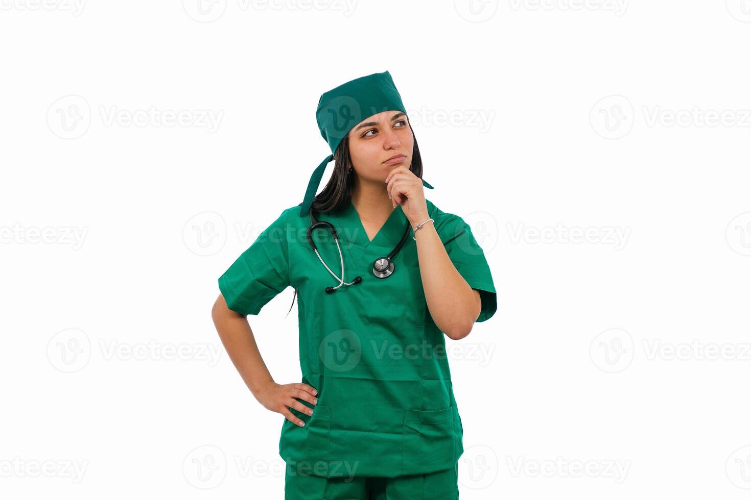 Pensive latin surgeon wearing green scrubs and stethoscope is thinking with hand on chin photo