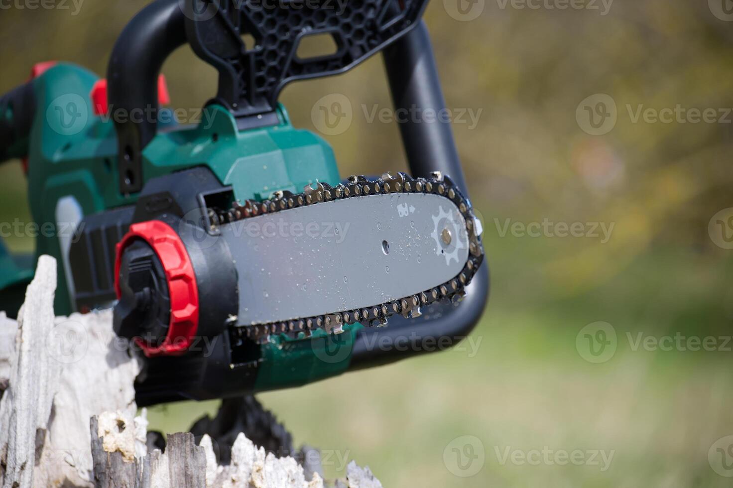Close-up shot of a modern, battery-powered chainsaw resting on a weathered stump. photo