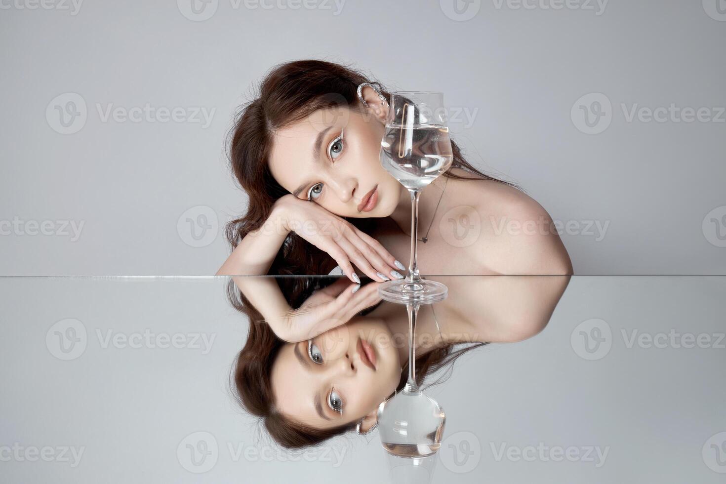 Reflection a woman in mirror with glass in her hand. Beautiful face makeup, natural cosmetics photo