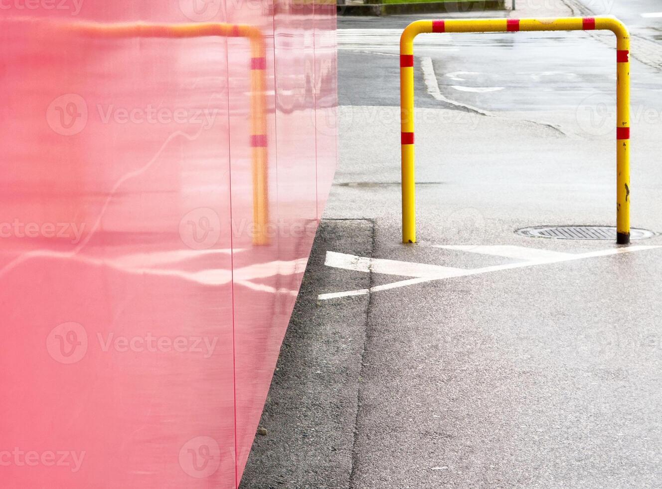 Urban scene with red wall, wet pavement, and yellow safety rail on rainy day photo