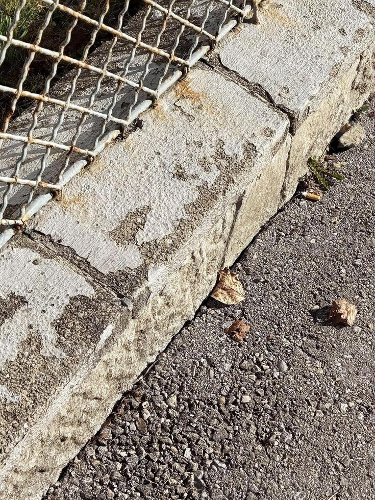 Weathered concrete and metal fence with fallen leaves on pavement photo