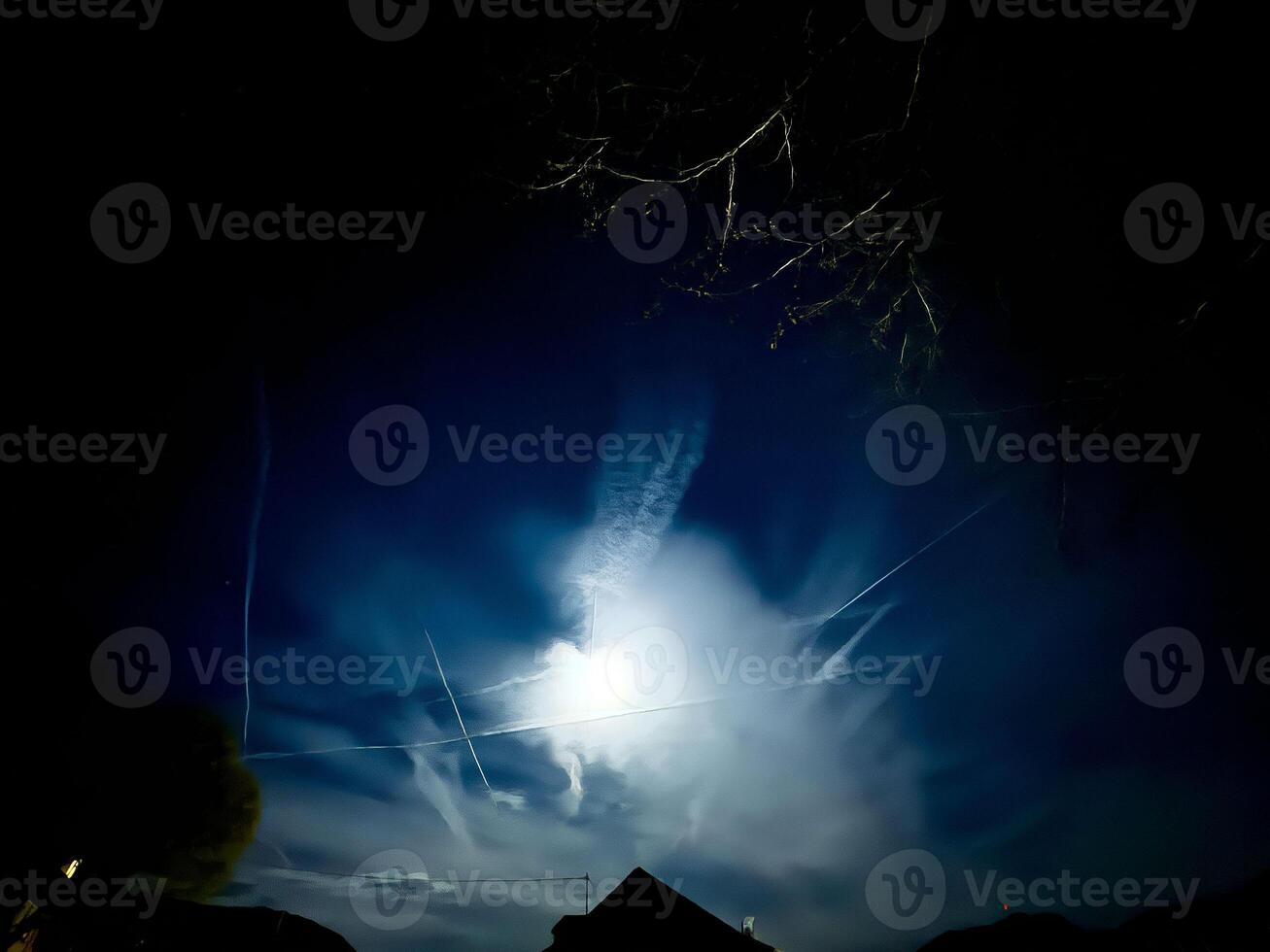 Night sky with bright moon and dramatic clouds illuminated in silhouette photo