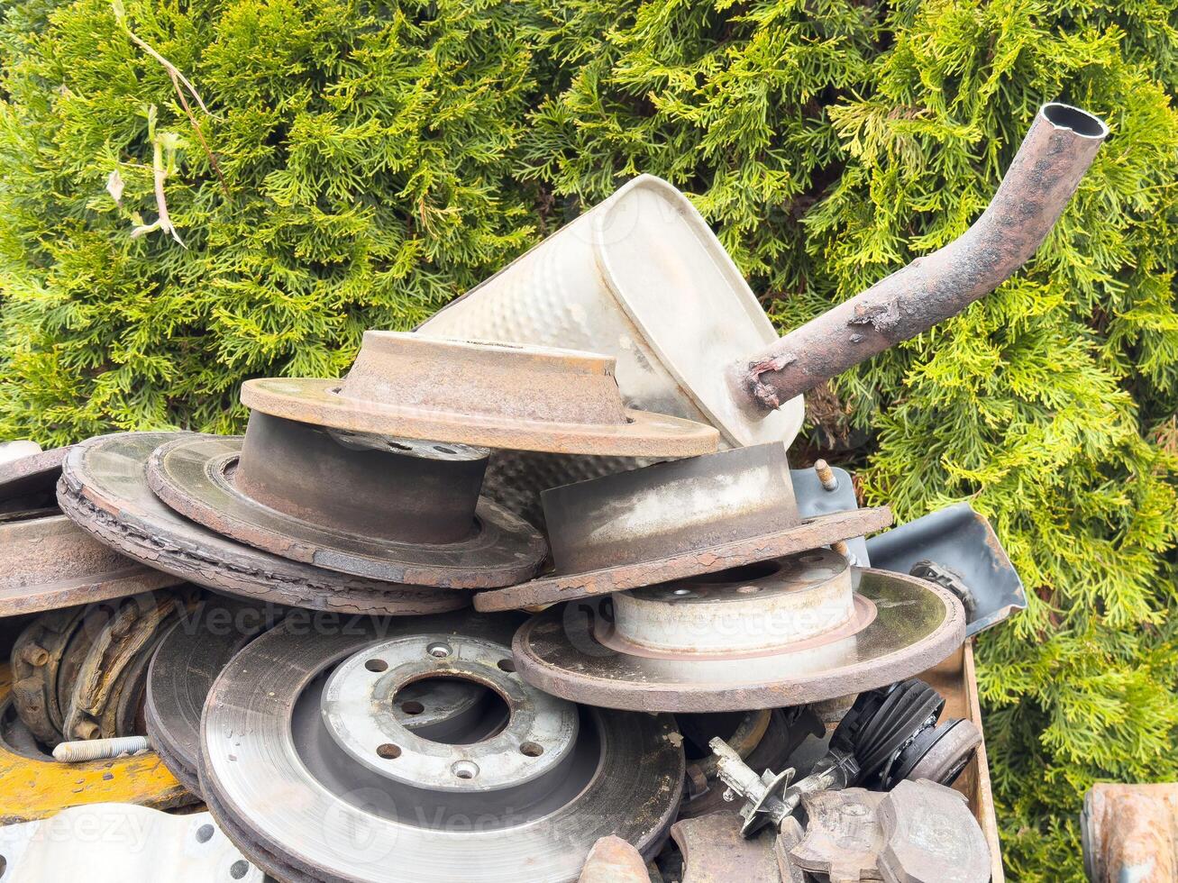 Rusty car parts pile with greenery background in outdoor setting photo