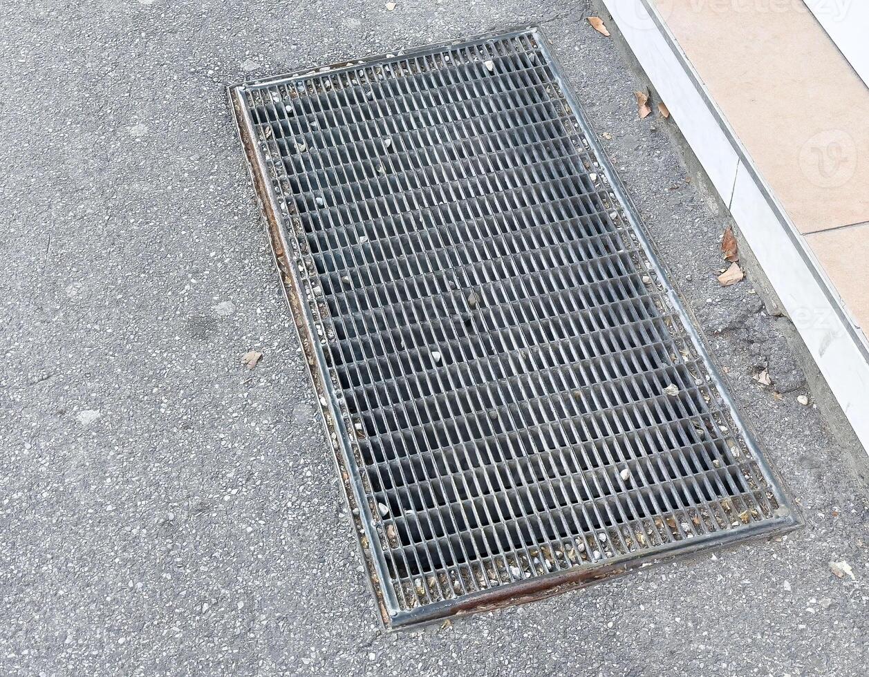 Metal grate on pavement surface adjoining sidewalk with leaves and debris photo