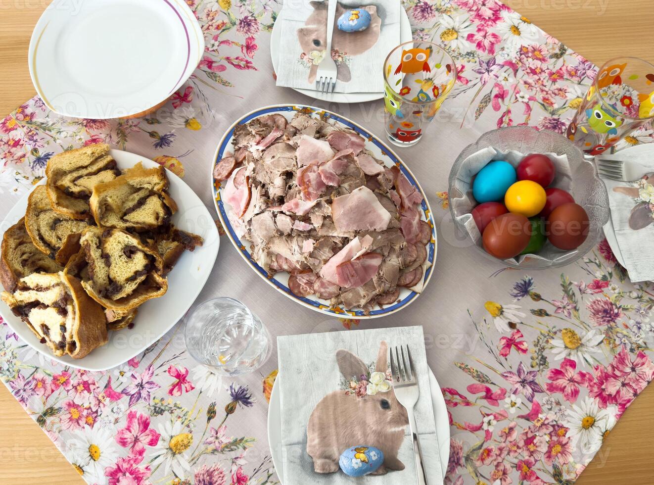 Easter brunch table with sliced meat, pastries, and colored eggs on floral tablecloth photo