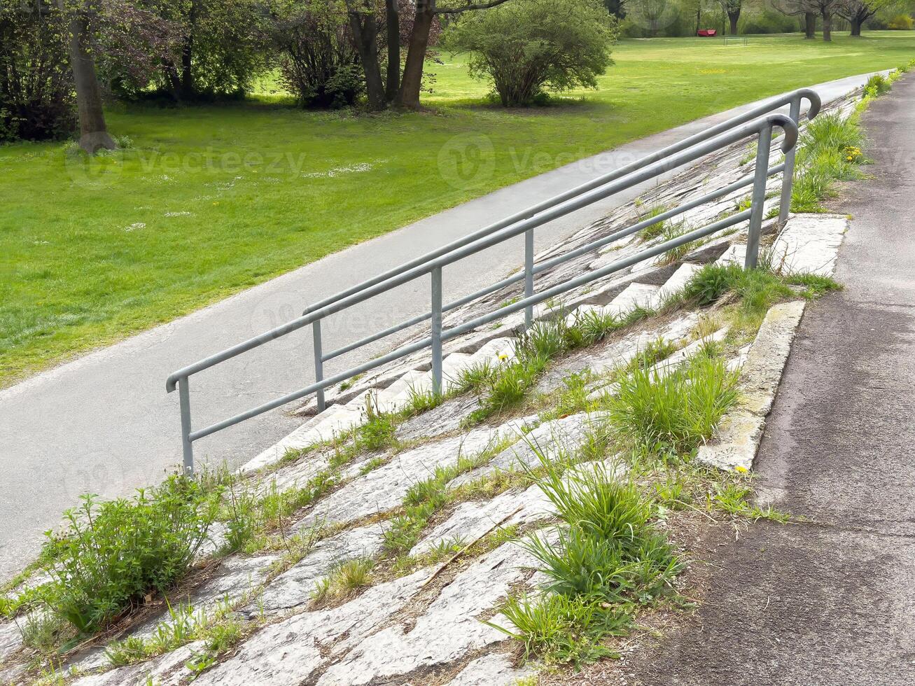 Park path with metal railing and overgrown grass in spring photo