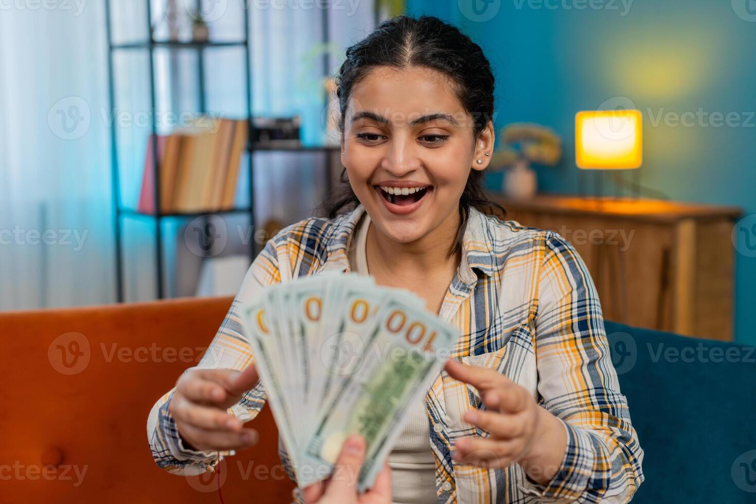 Sudden happiness Indian woman joyfully celebrating receiving plenty cash dollar showing victory sign photo