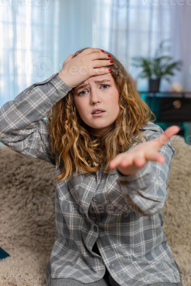 Woman sits on sofa making facepalm gesture feeling disappointed frustrated after unexpected failure photo