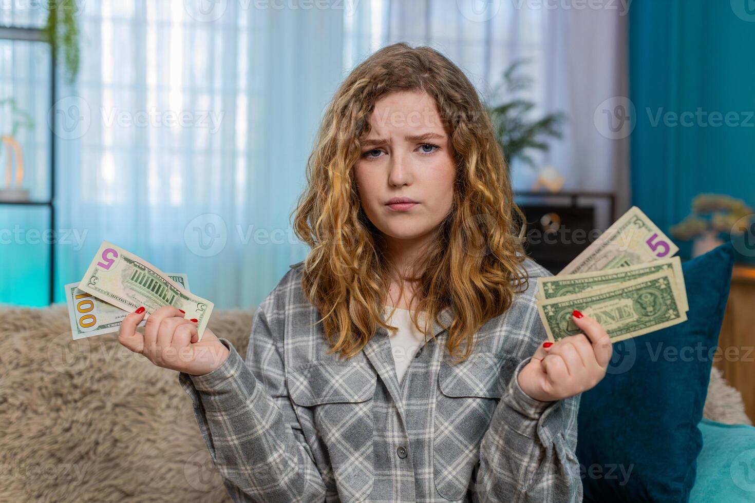 Woman sitting on sofa counting cash dollars in hands feeling satisfied or worried about money issues photo