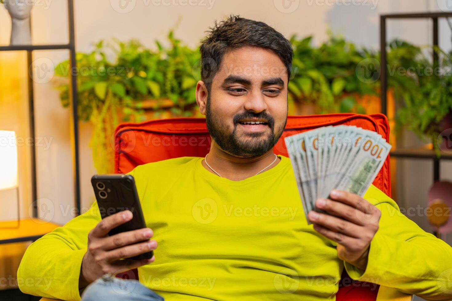 Rich happy Indian man counting money cash on smartphone calculator app, calculate income earnings photo