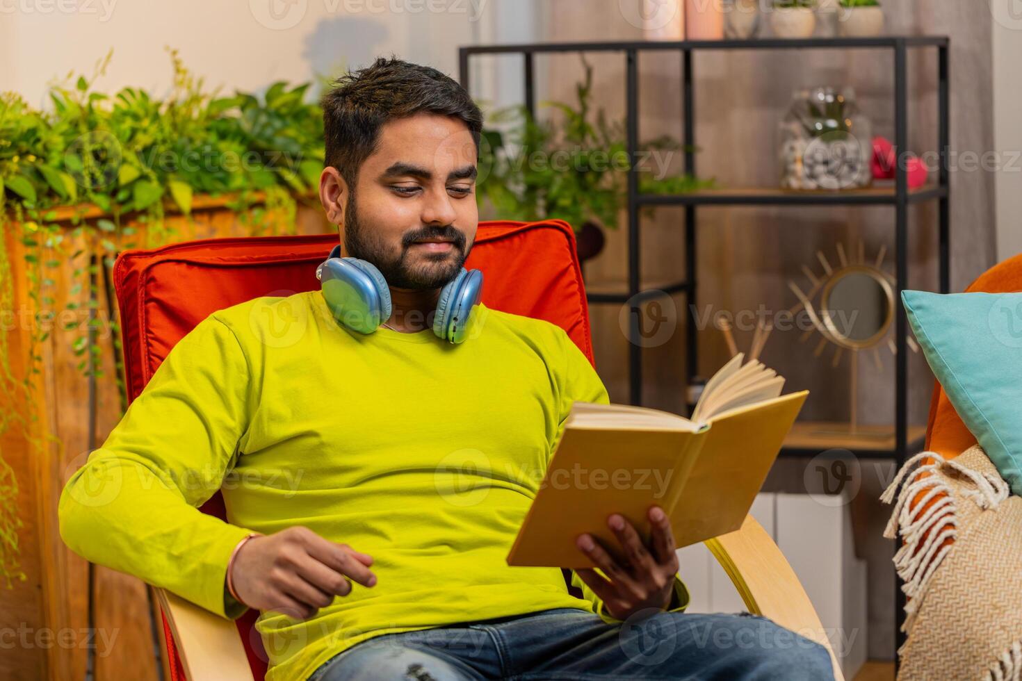 Indian man reading interesting book turning pages smiling enjoying literature taking a rest on chair photo