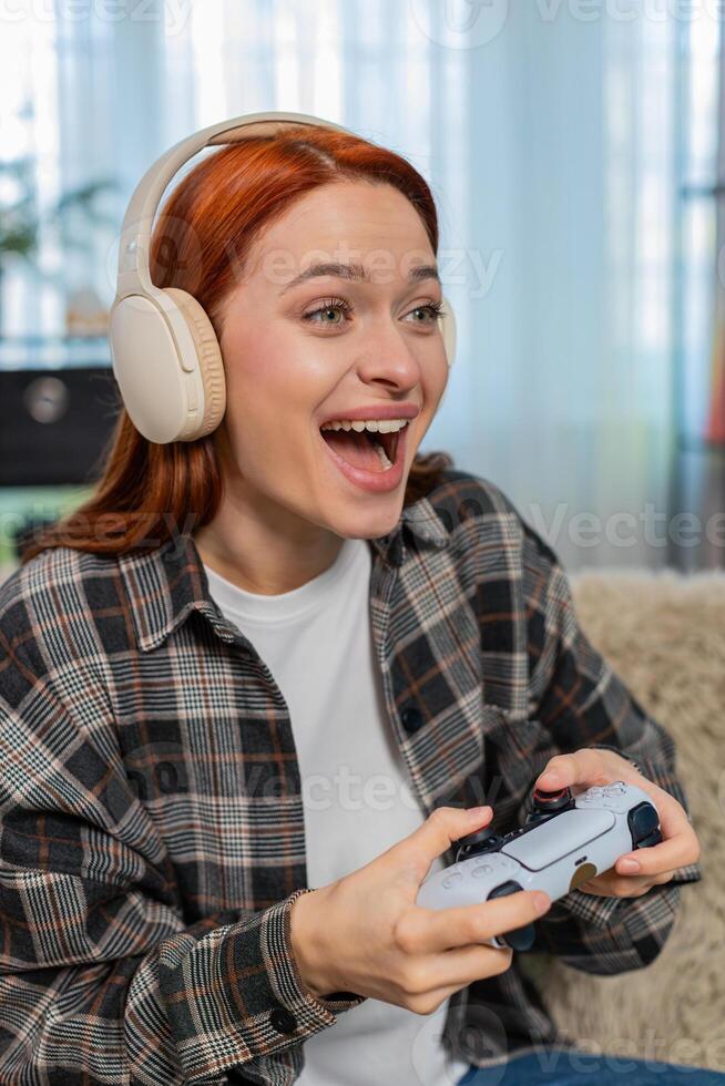 Young woman on sofa playing game with joystick emotionally reacting to action on screen photo