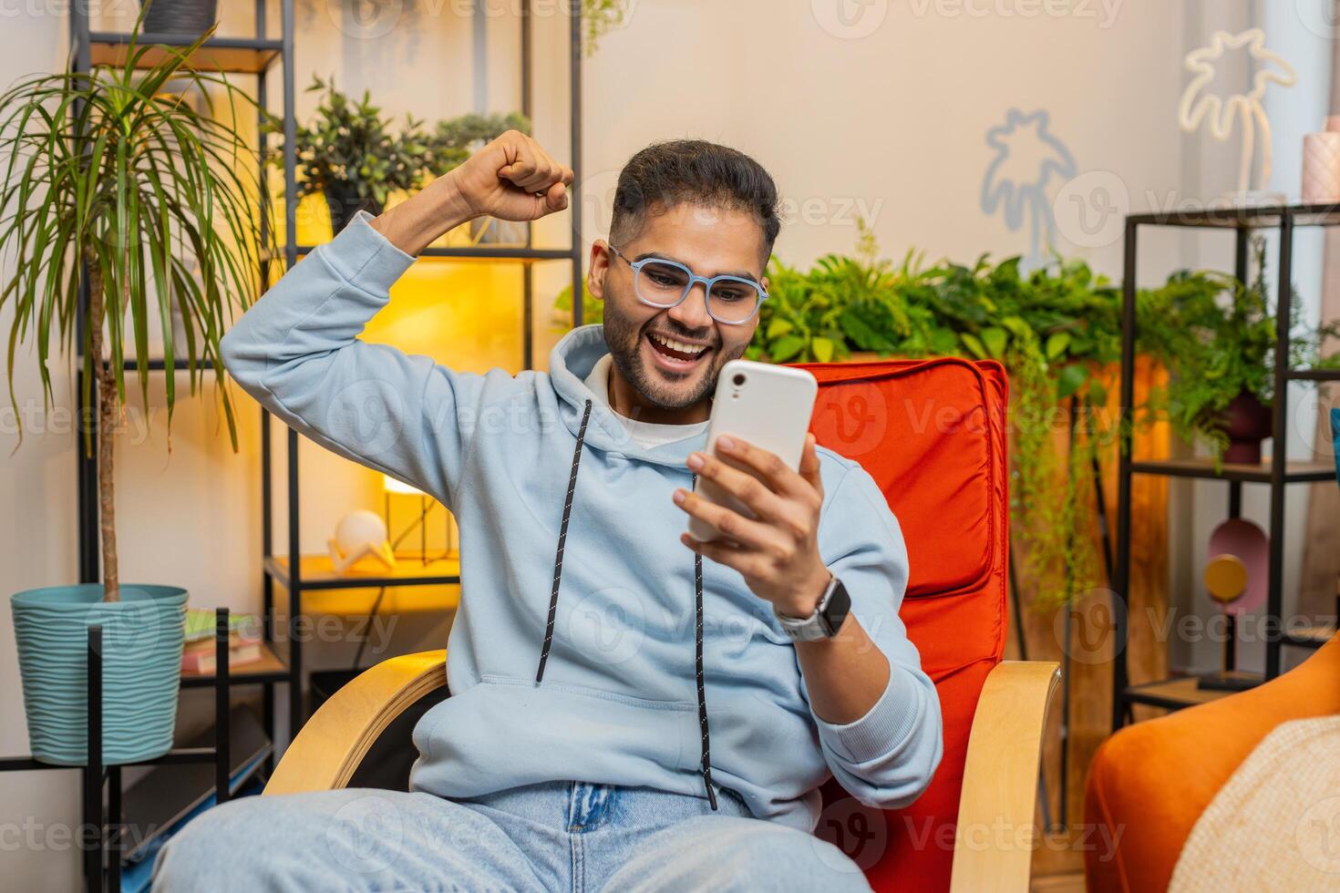 Indian Arabian man at home room use smartphone celebrating success victory winning play online games photo