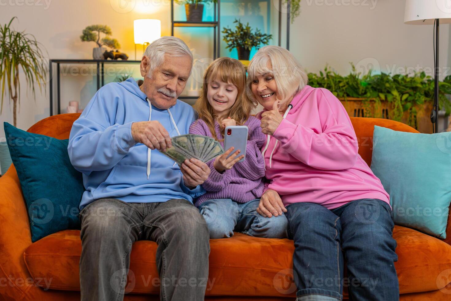 Child girl granddaughter with grandparents counting money using smartphone calculator at home photo