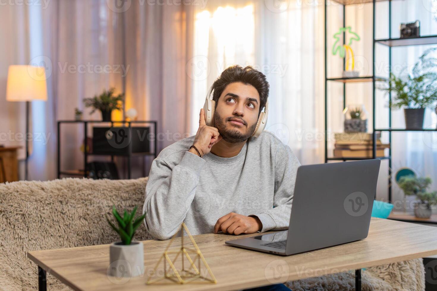 Young Indian man wearing wireless headphones working on laptop while listening to audiobook at home photo