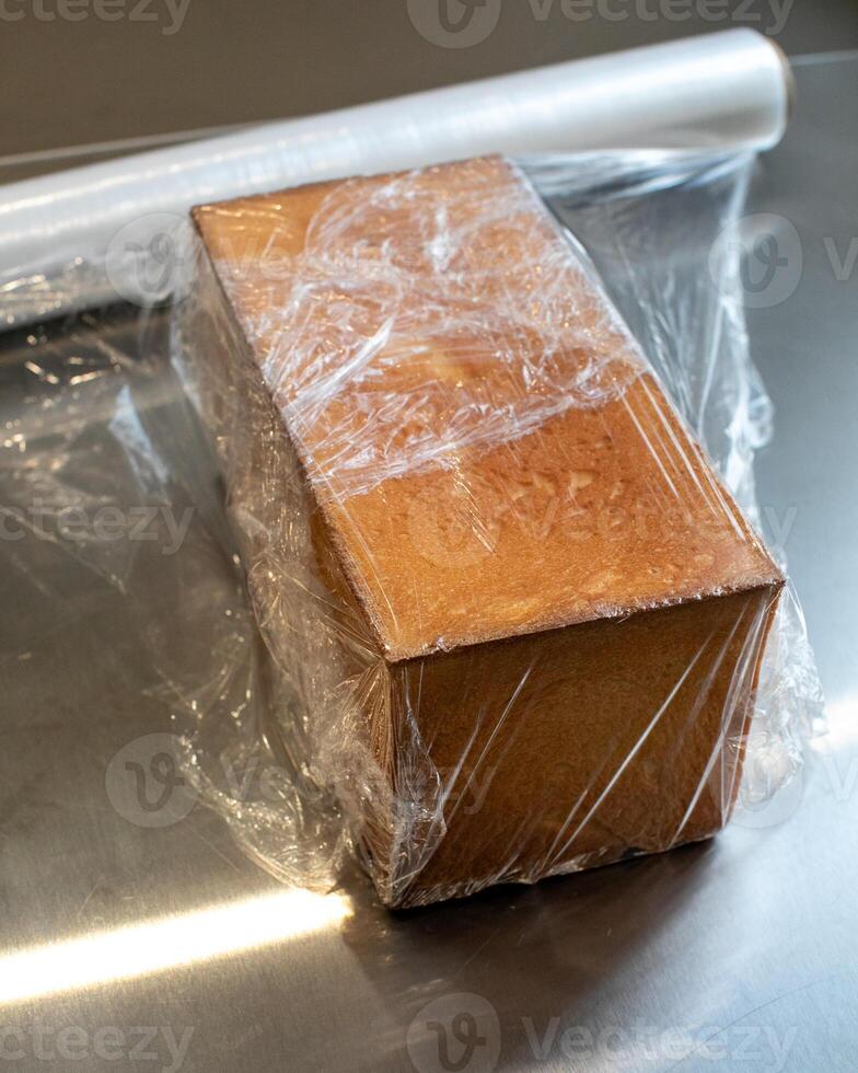 Golden brown bread loaf wrapped in plastic, fresh bakery packaging, sustainable food storage, kitchen essentials, homemade bread preparation photo