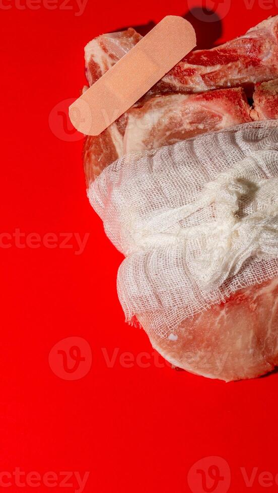 Raw meat wrapped with bandage and plaster on vivid red, highlighting food safety and unconventional healing concept photo