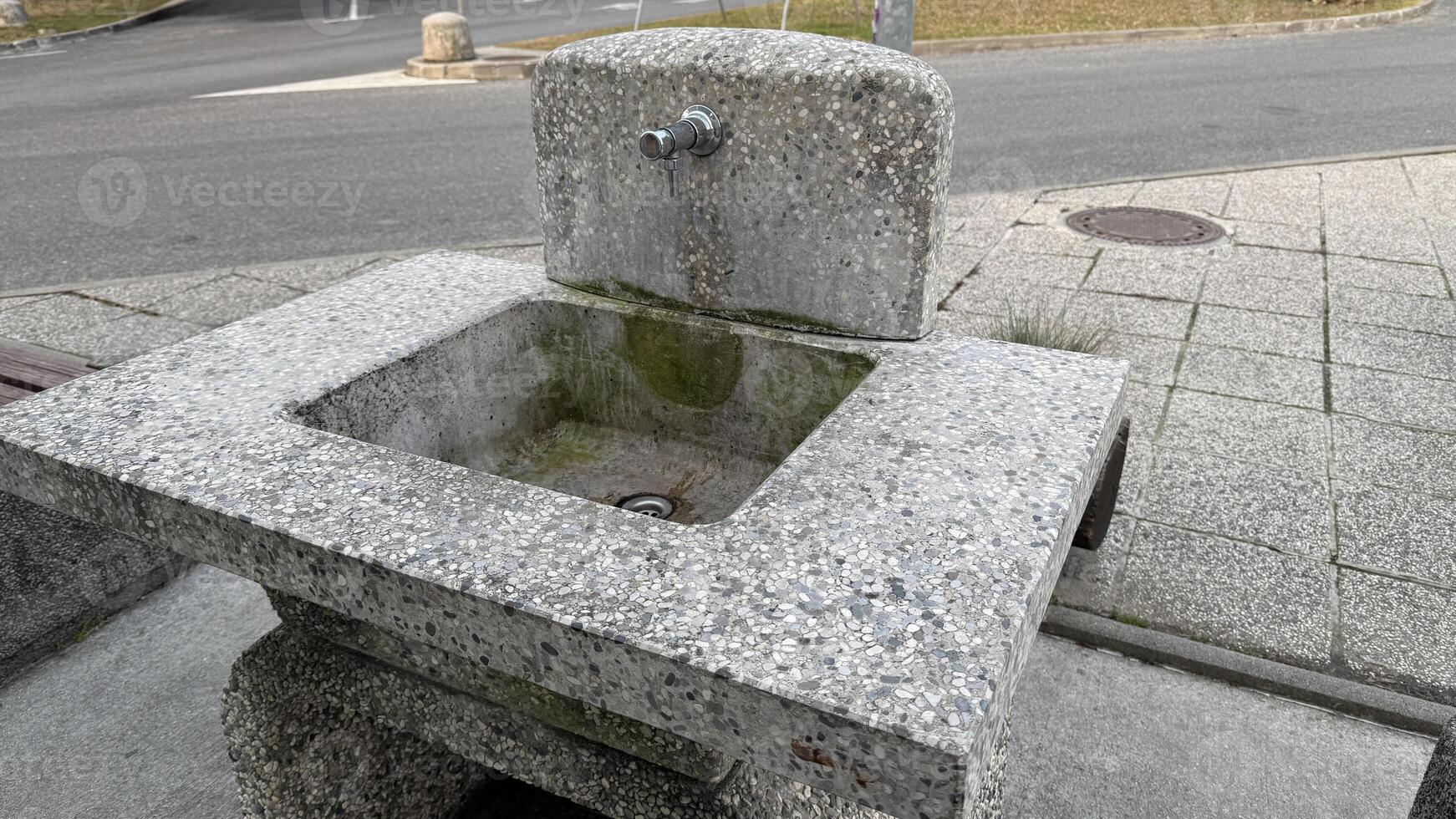 Stone outdoor sink on urban pavement, public water source, rustic architecture, travel destination, environmental sustainability, city park amenity photo