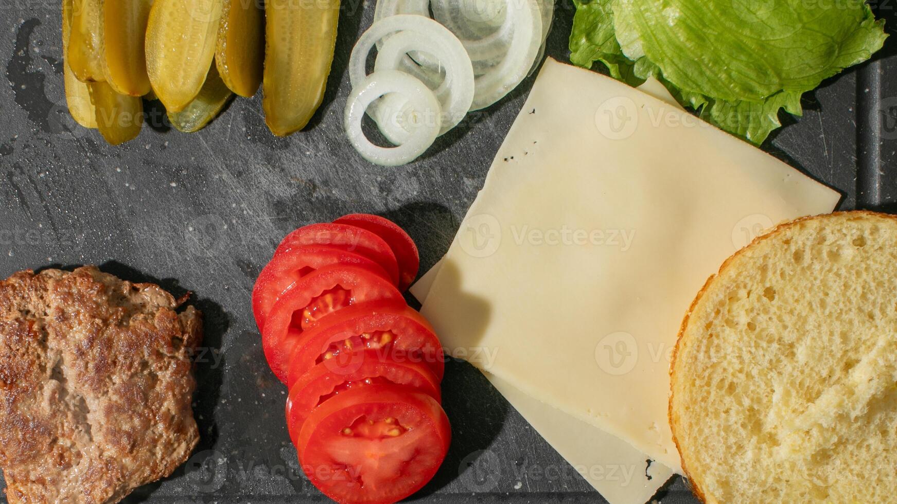 Burger ingredients arranged on a dark surface, featuring fresh veggies and cheese, ideal for summer cookouts and barbecues photo