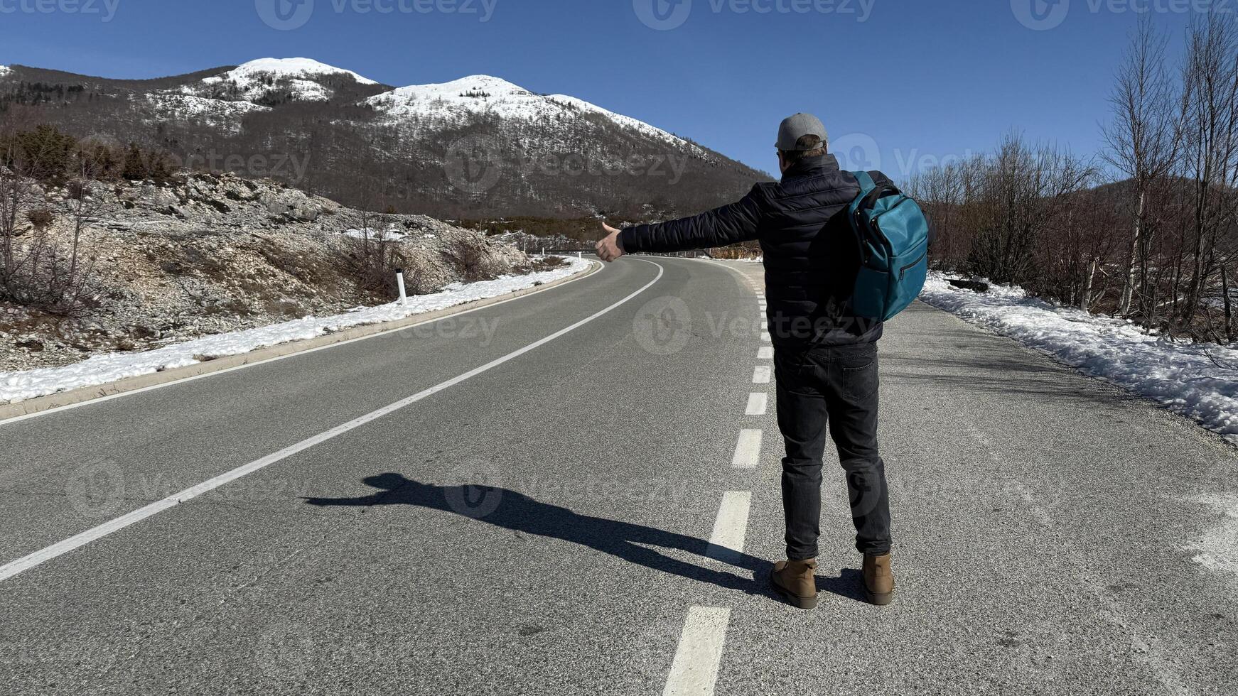 Middle aged Caucasian man hitchhiking on a rural winter road, adventure travel and New Year exploration themes photo