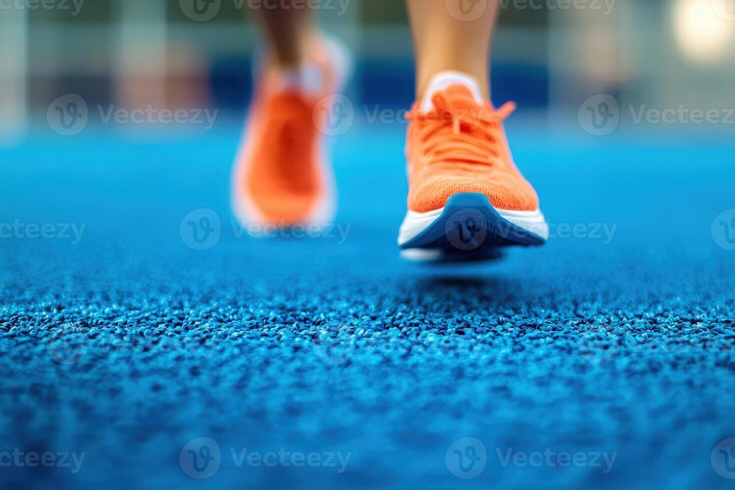 A close-up view of bright orange running shoes hitting a textured blue track surface. The focus highlights the runners motion and determination during an intense training session. photo