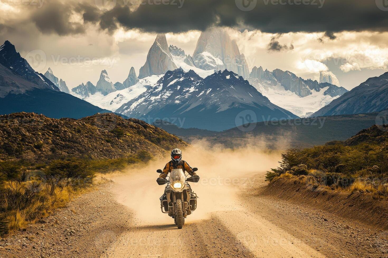 A motorcyclist rides through a dusty path in Patagonia, with majestic mountains and glaciers in the background. The atmosphere is charged, showcasing natures grandeur and the thrill of exploration. photo