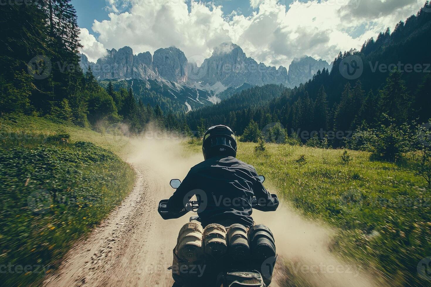 A rider navigates a rugged dirt path in a lush, green landscape with majestic mountains in the background. photo