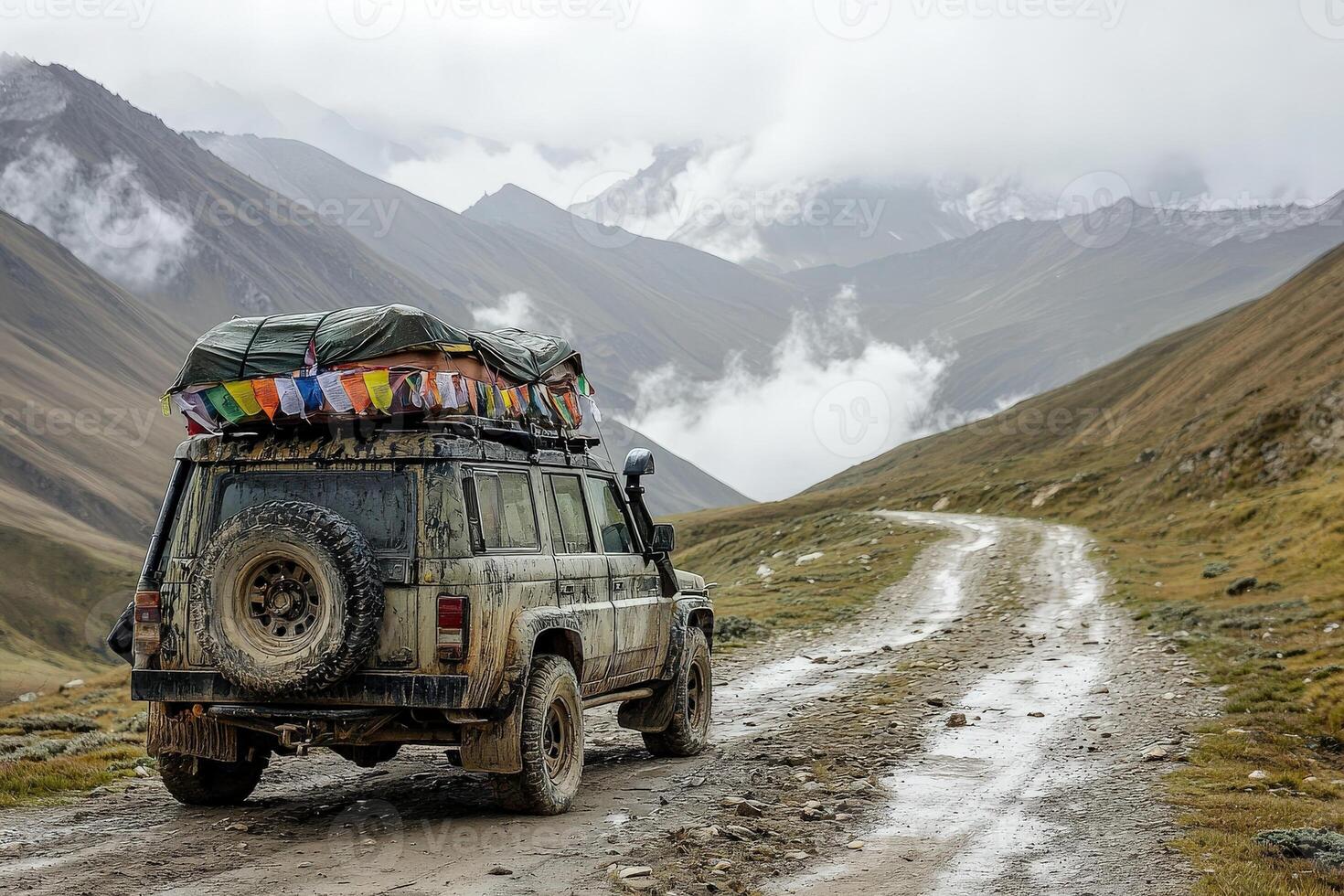 An off-road vehicle is parked on a winding dirt road surrounded by majestic mountains. Colorful flags adorn the roof, hinting at a journey through wild landscapes. photo