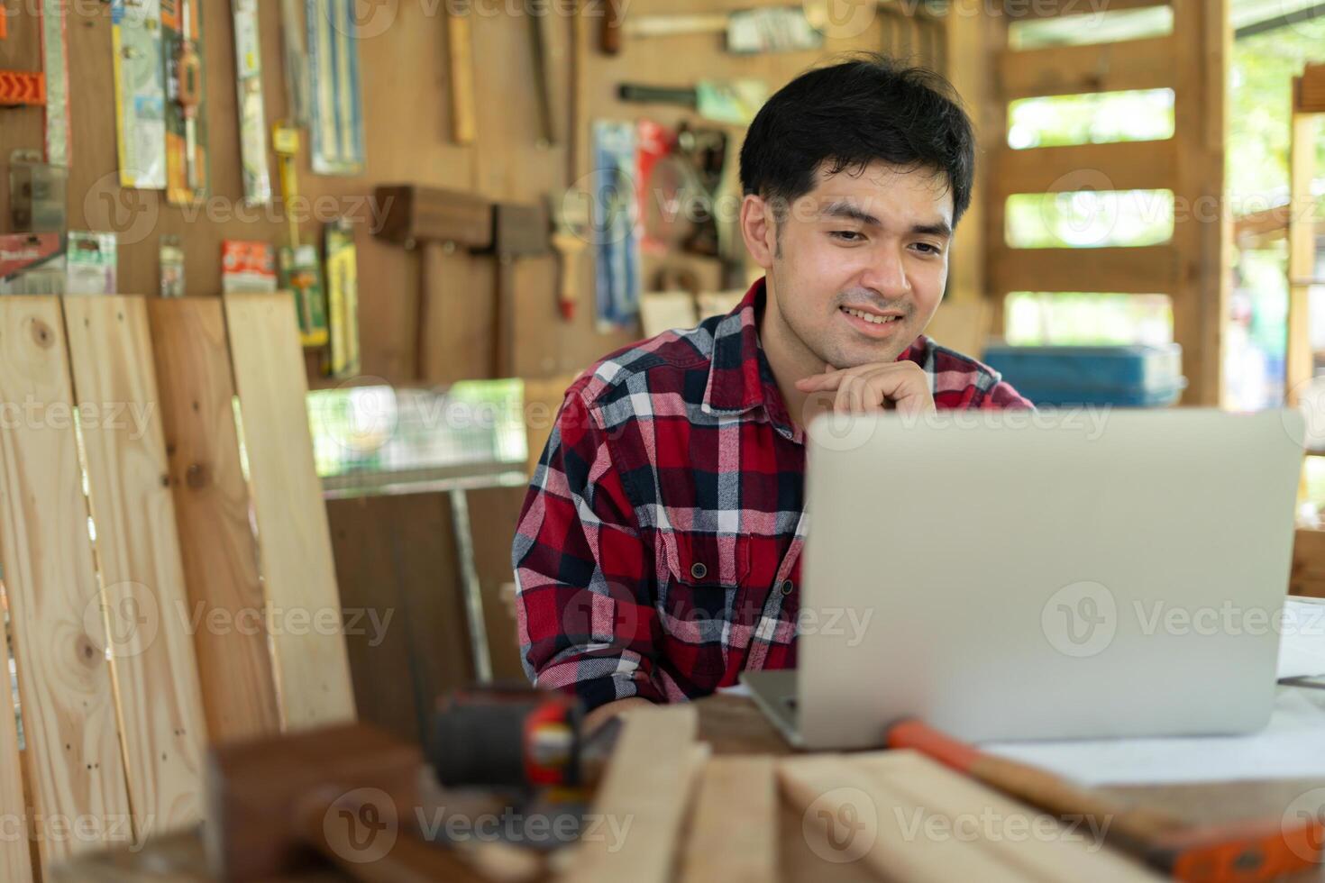 Asian man owner a small furniture business is recheck order online. carpenter male is adjust wood to the desired size. architect, designer, Built-in, professional wood, craftsman, workshop photo