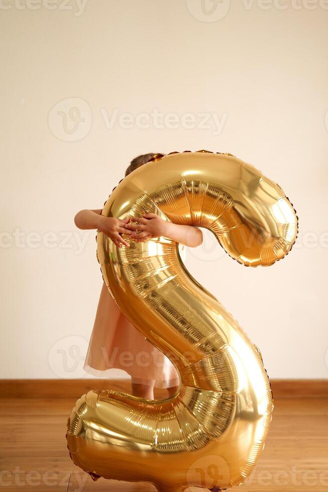 Little girl is standing in a room hugging an inflatable number 2 photo