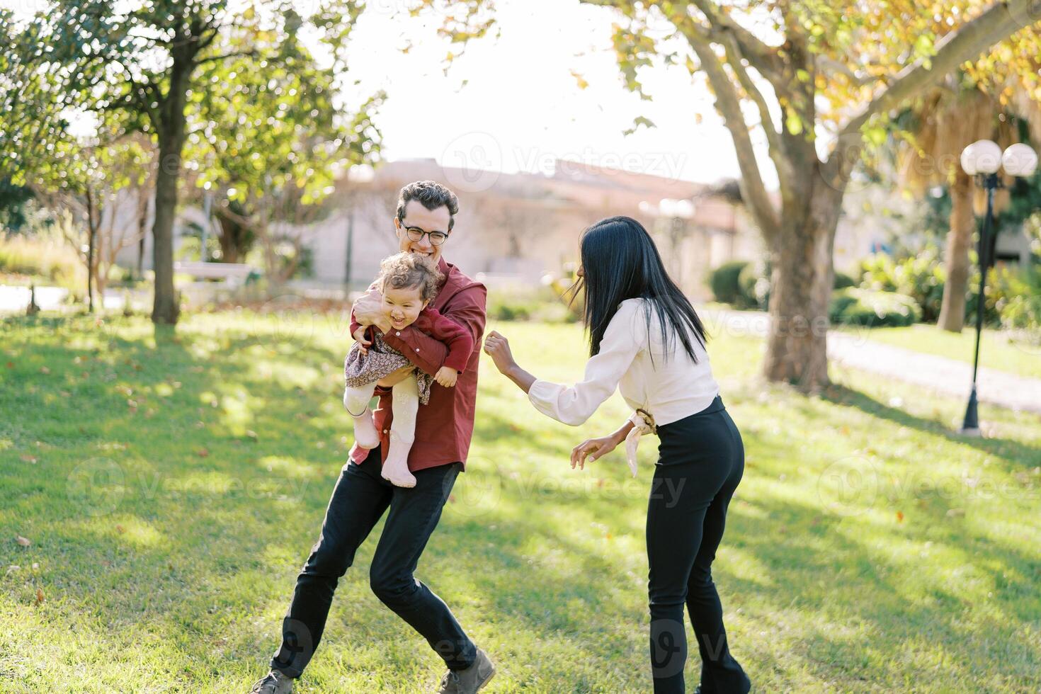 Laughing dad runs around mom with a little girl in his arms photo