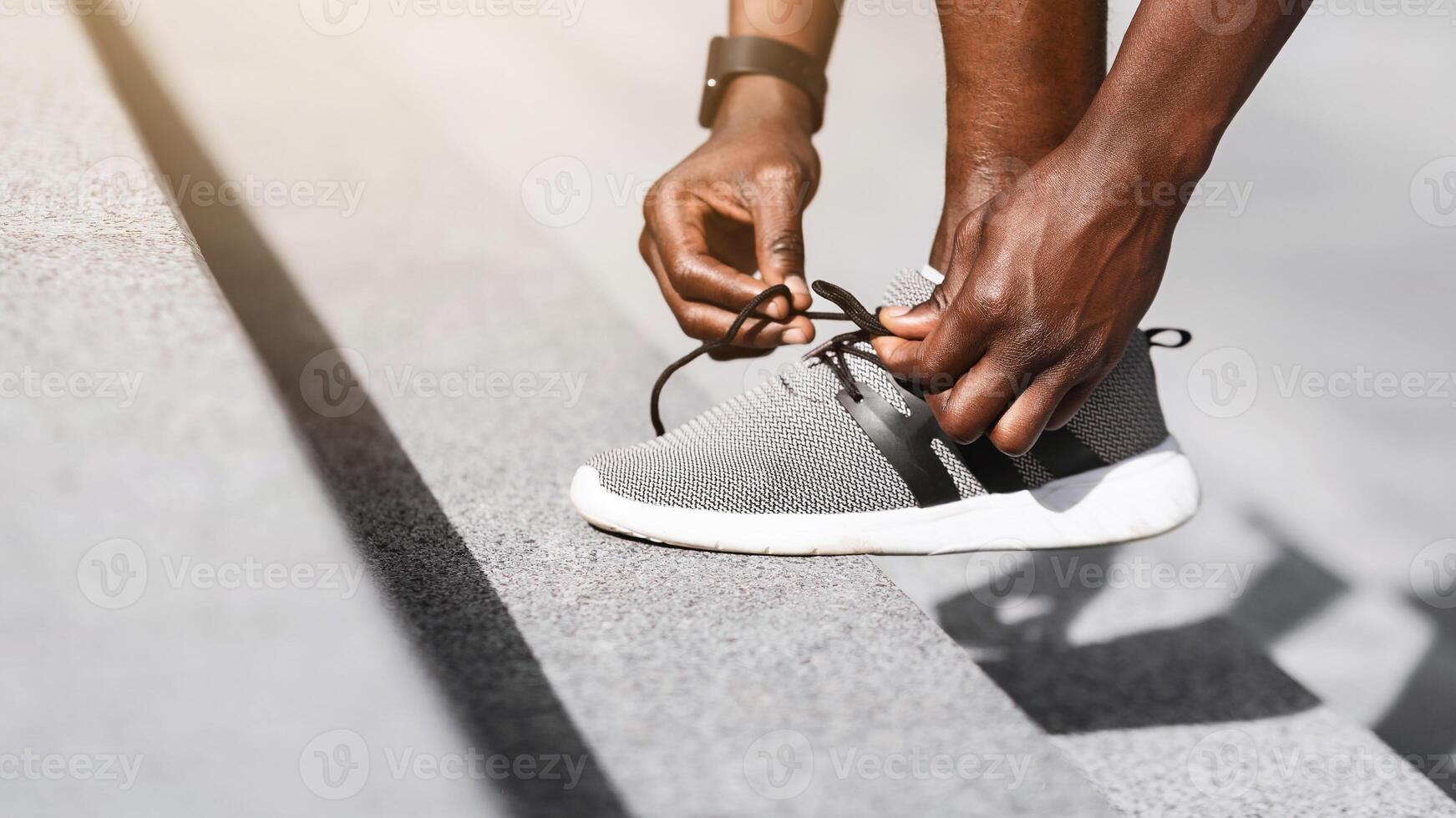 Black sportsman tying shoelaces before running, getting ready for jogging outdoors, putting leg at steps, cropped image with copy space, side view photo