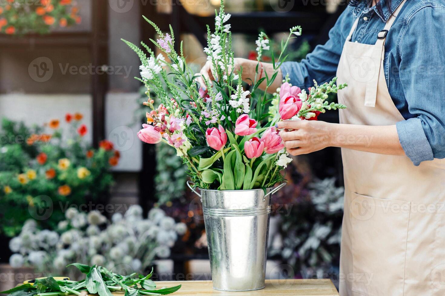 Florist at work, pretty young woman making trendy modern bouquet of different flowers. Young designer in protective mask and apron makes composition for client during covid-19 epidemic, copy space photo