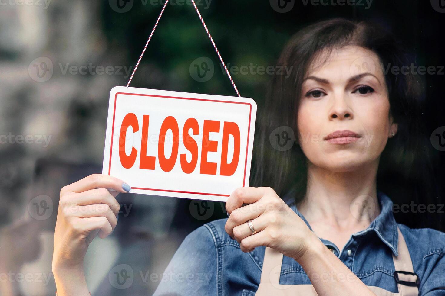COVID-19 outbreak and closure of small businesses during lockdown, store problems. Sad young female in apron turns sign with inscription is closed in flower studio with beautiful plants, copy space photo