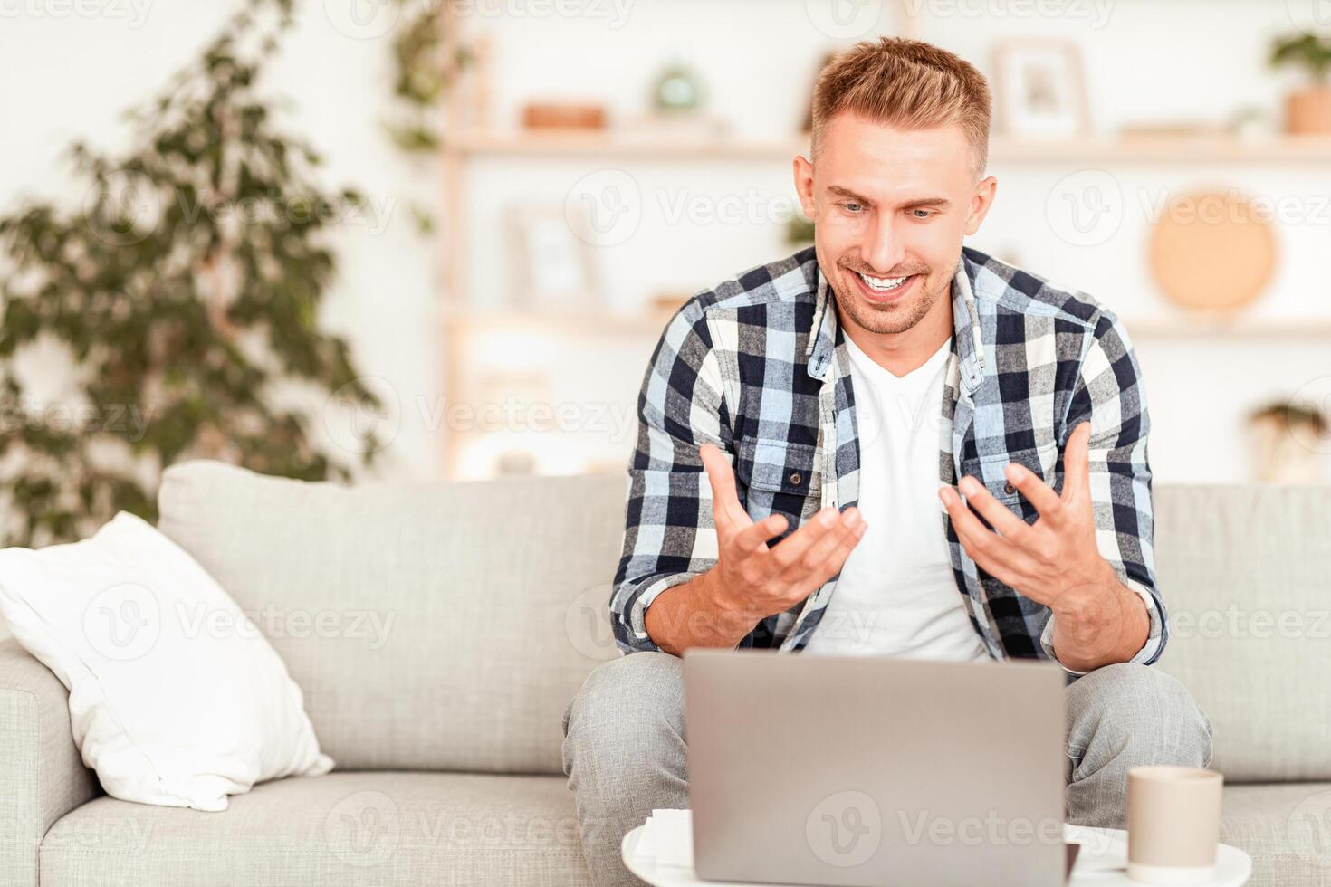 Virtual Conversation. Portrait of young manager having online call on laptop, talking to webcam. Cheerful man explaining something to client and gesturing, sitting on the sofa at his house photo