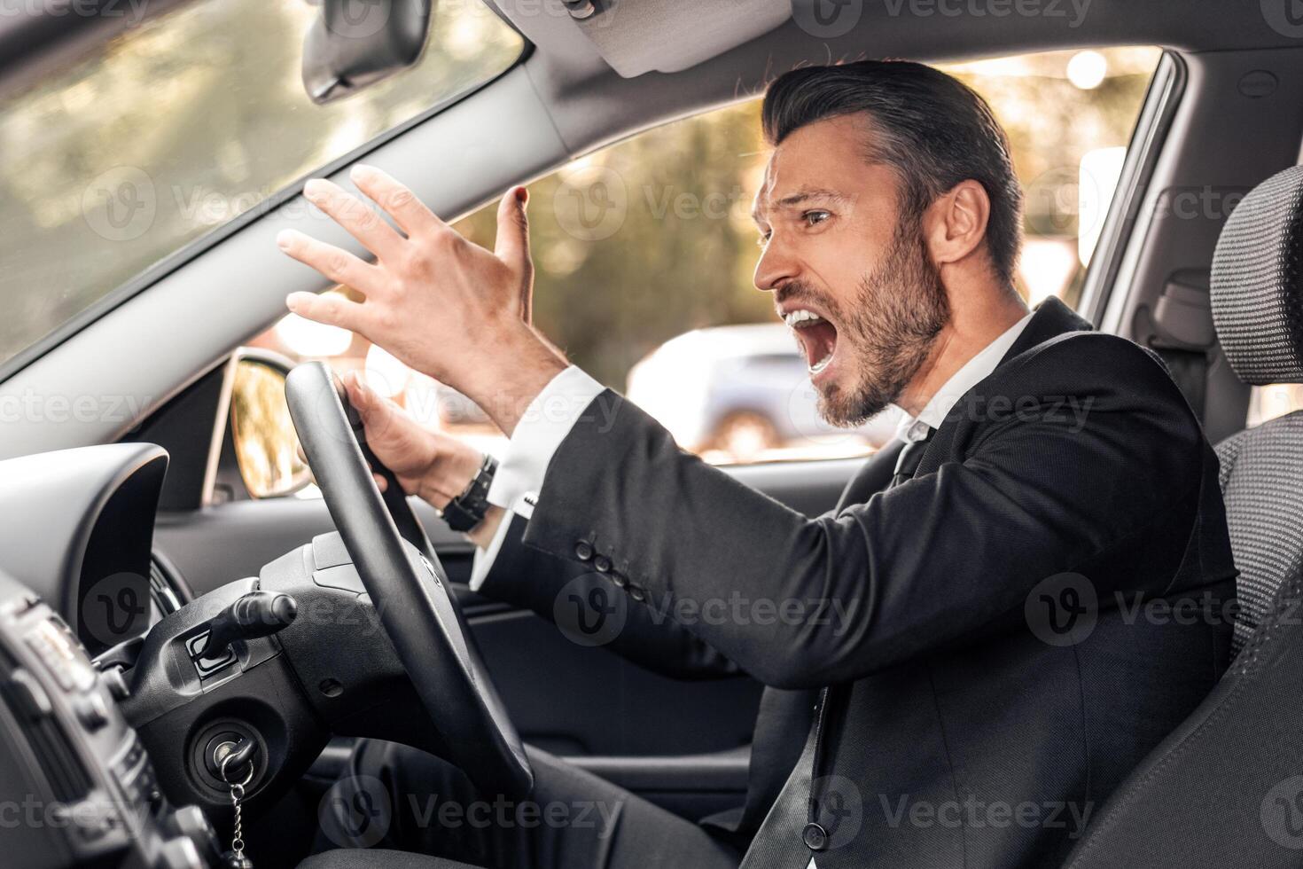 Stressed businessman driving luxury car, stuck in traffic, late to airport, side view, copy space. Furious middle-aged man in expensive suit screaming and gesturing while driving auto photo