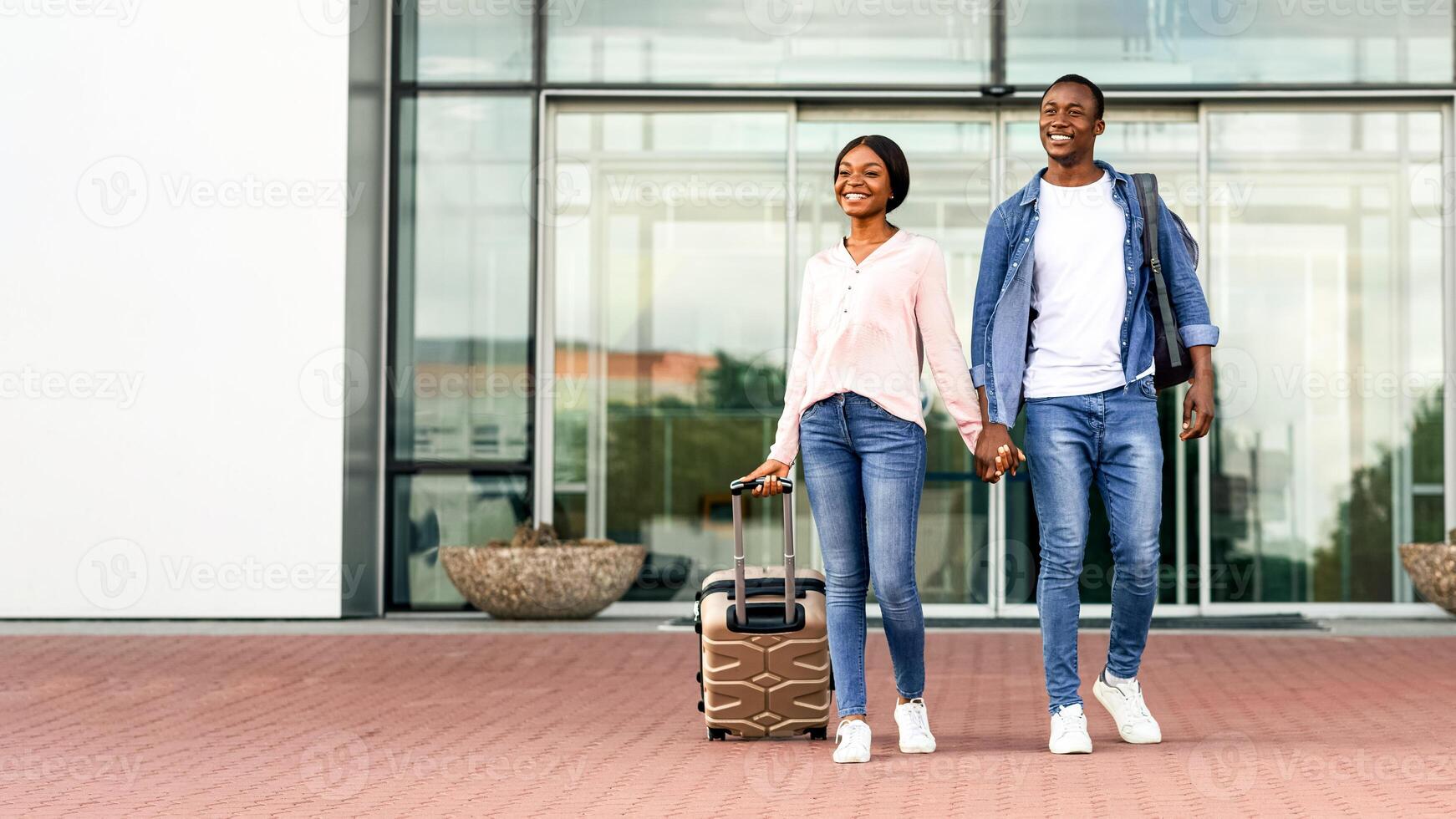 Portrait Of Happy African American Couple Leaving Airport Building After Arrival, Going Out Of Terminal, Holding Hands And Smiling, Excited Black Spouses Enjoying Travelling Together, Free Space photo