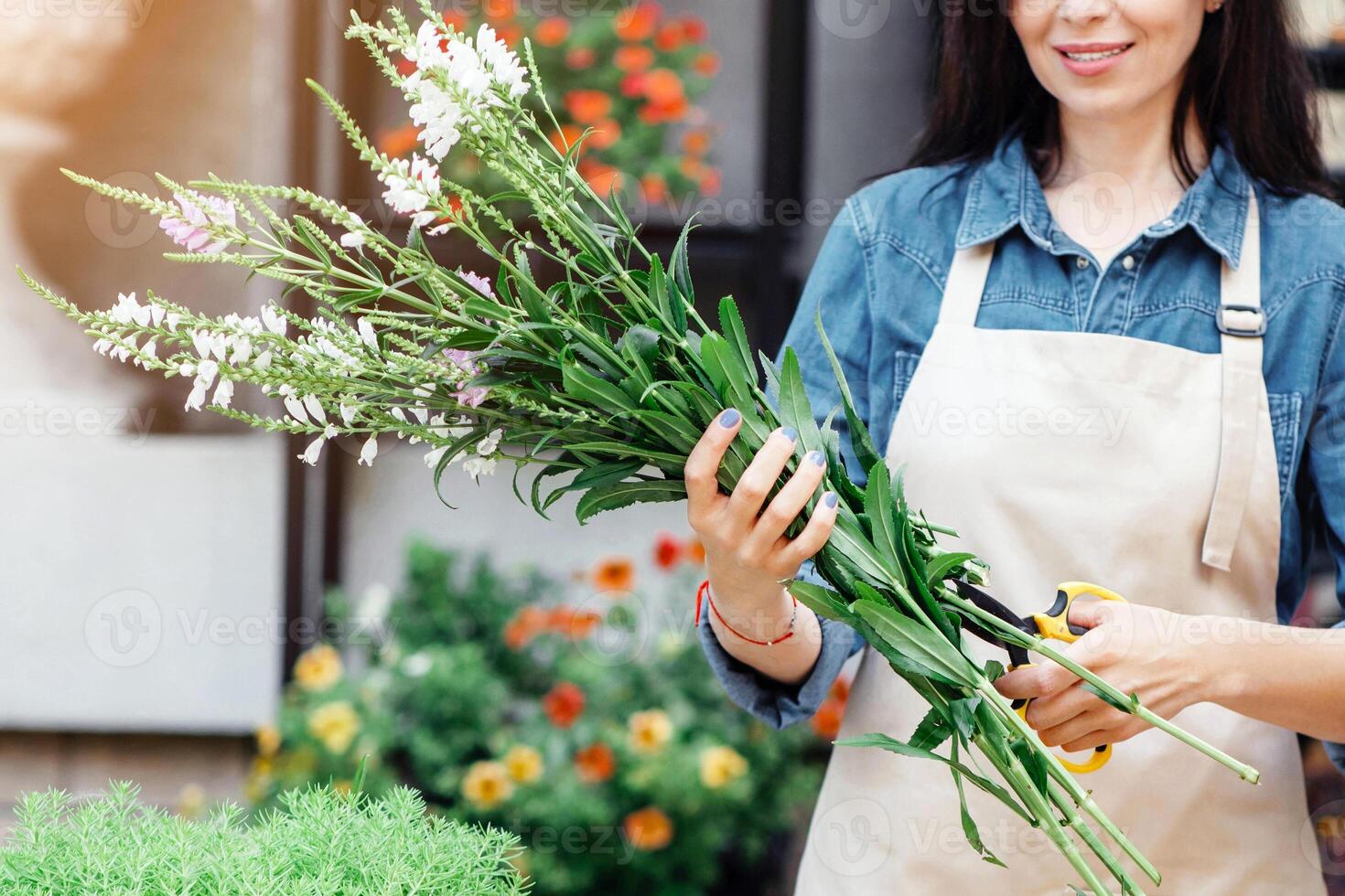 Nice business lady, seller creating fresh new order, gift designer on desk, hobby and creative work at flower shop. Smiling young female in apron trims plants for bouquet behind counter at shop photo