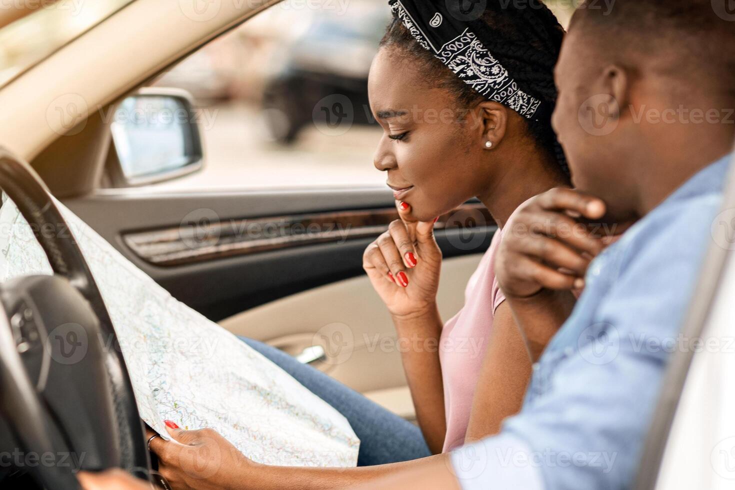 GPS, location, map, navigation concept. Confused young black family travelling by car together, got lost, checking paper map, looking for appropriate way to destination, side view, copy space photo