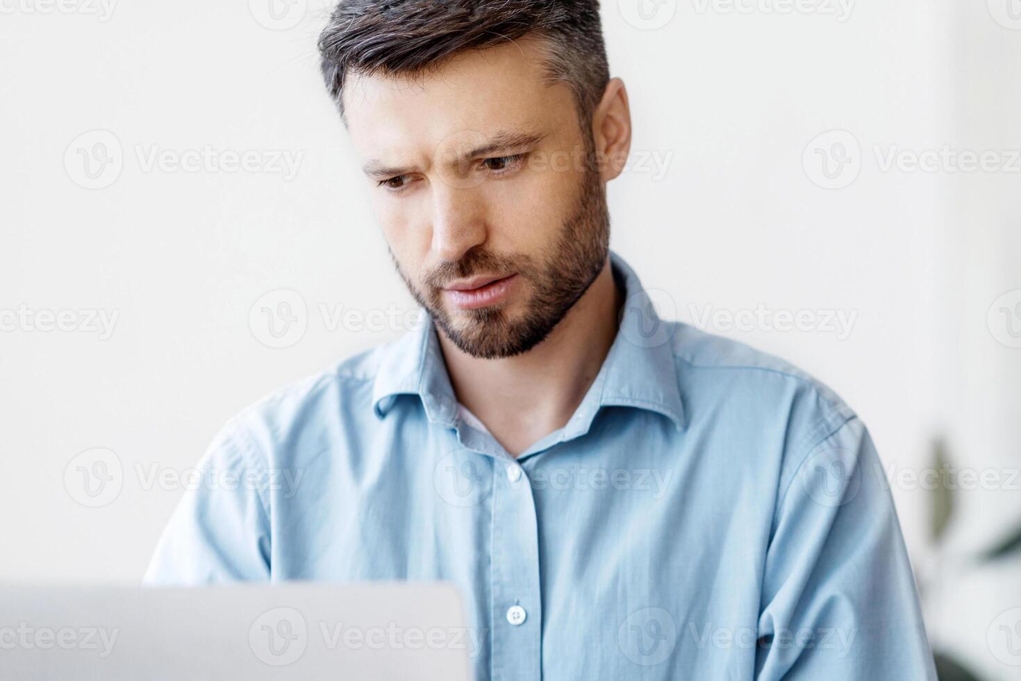 Concentrated businessman working on laptop at workplace in office, male entrepreneur looking at computer screen and typing on keyboard, filling report, answering emails, managing project, copy space photo