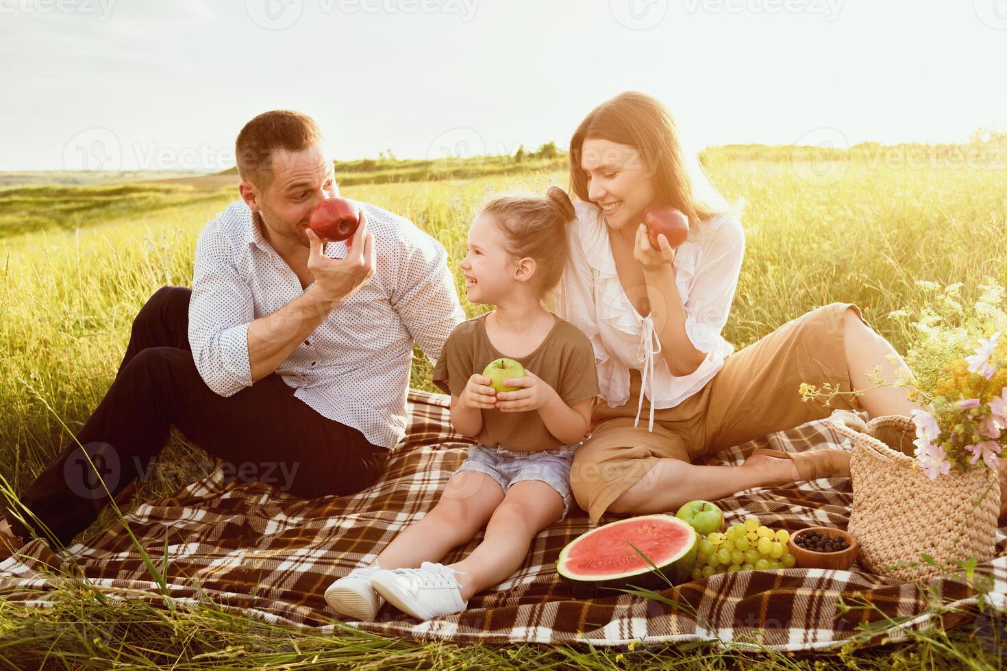 Fooling Around. Cheerful family resting on the blanket, eating and playing with apples photo