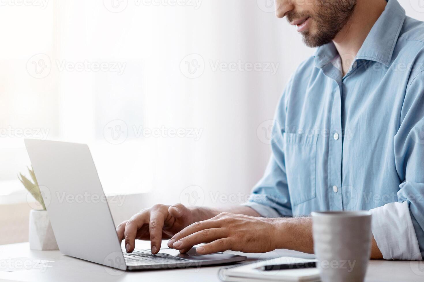 Handsome Male Freelancer Working On Laptop At Desk In Home Office, Answering Emails, Typing On Computer Keyboard, Communicating With Clients, Enjoying Remote Work, Side View With Copy Space photo