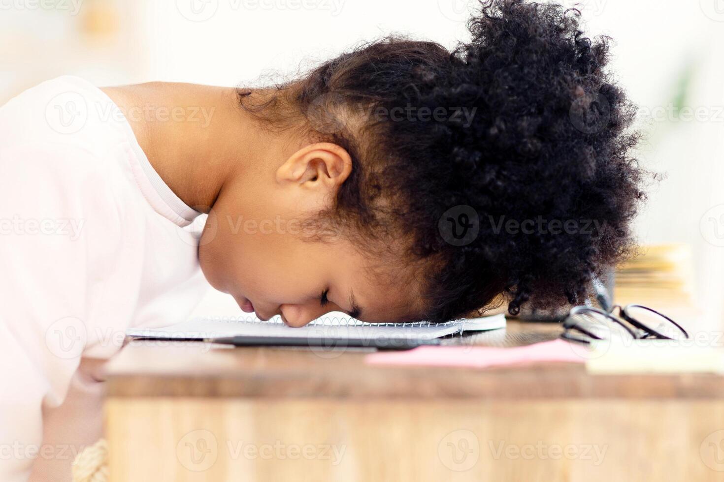 Overworked African Girl Resting Head On Desk Tired Of Homework And Distant School Education Sitting Indoor photo