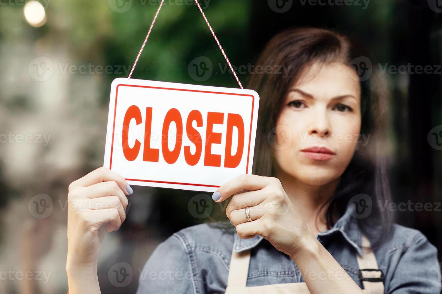 Problems in small business, coronacrisis, closure of cafes, salons and shops during COVID-19 lockdown. Sad millennial female in apron turns sign with inscription is closed, on door in flower studio photo