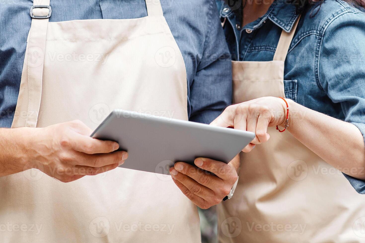 Flower shop, small business and delivery of bouquet during covid-19 lockdown. Young guy and woman in aprons and protective masks work with tablet and discussing online ordering near studio, copy space photo
