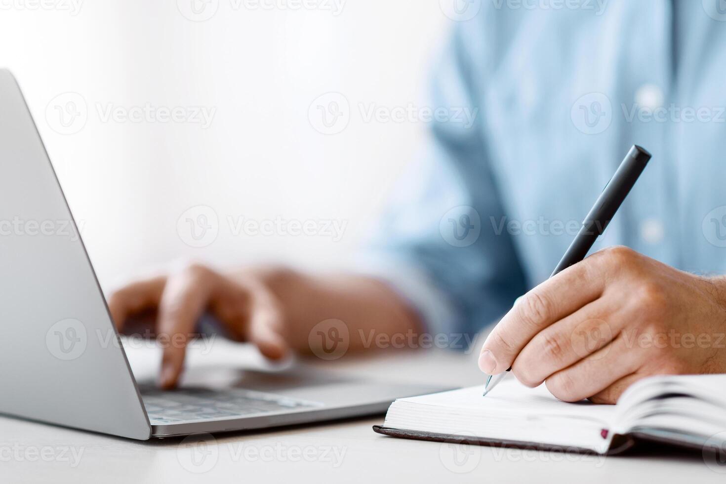Unrecognizable Man Writing In Notepad And Using Laptop In Office, Taking Notes At Workplace, Using Computer, Noting Information From Internet, Cropped Image With Selective Focus On Male Hand, Closeup photo