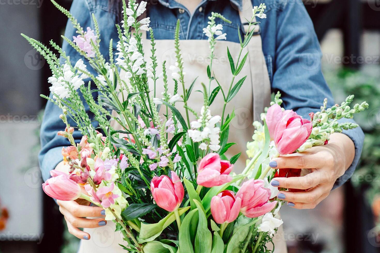 Modern flower arrangement and bouquet for delivery during social distancing. Young busy lady owner in apron and protective mask makes fashionable bouquet, in plant shop, empty space, outdoor photo