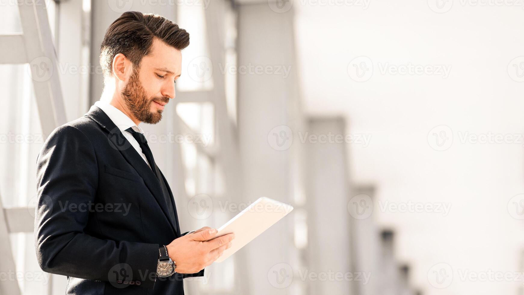Successful entrepreneur with digital tablet standing next to window in airport, using nice mobile application for business while waiting for flight, panorama with copy space, side view photo
