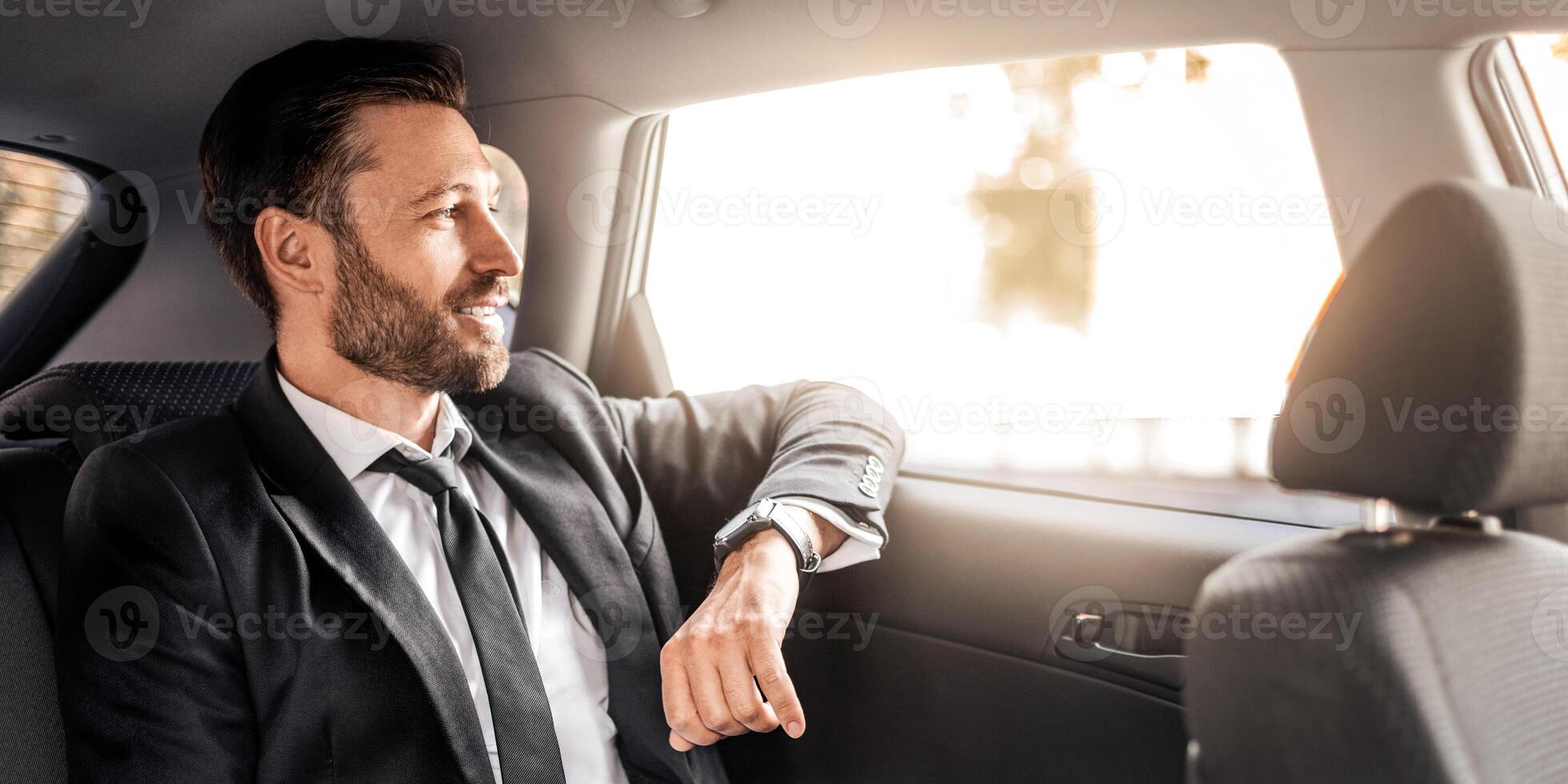 Successful businessman looking through window and smiling, going by car to meeting, thinking about business opportunities. Side view of handsome man sitting in luxury car, panorama with copy space photo