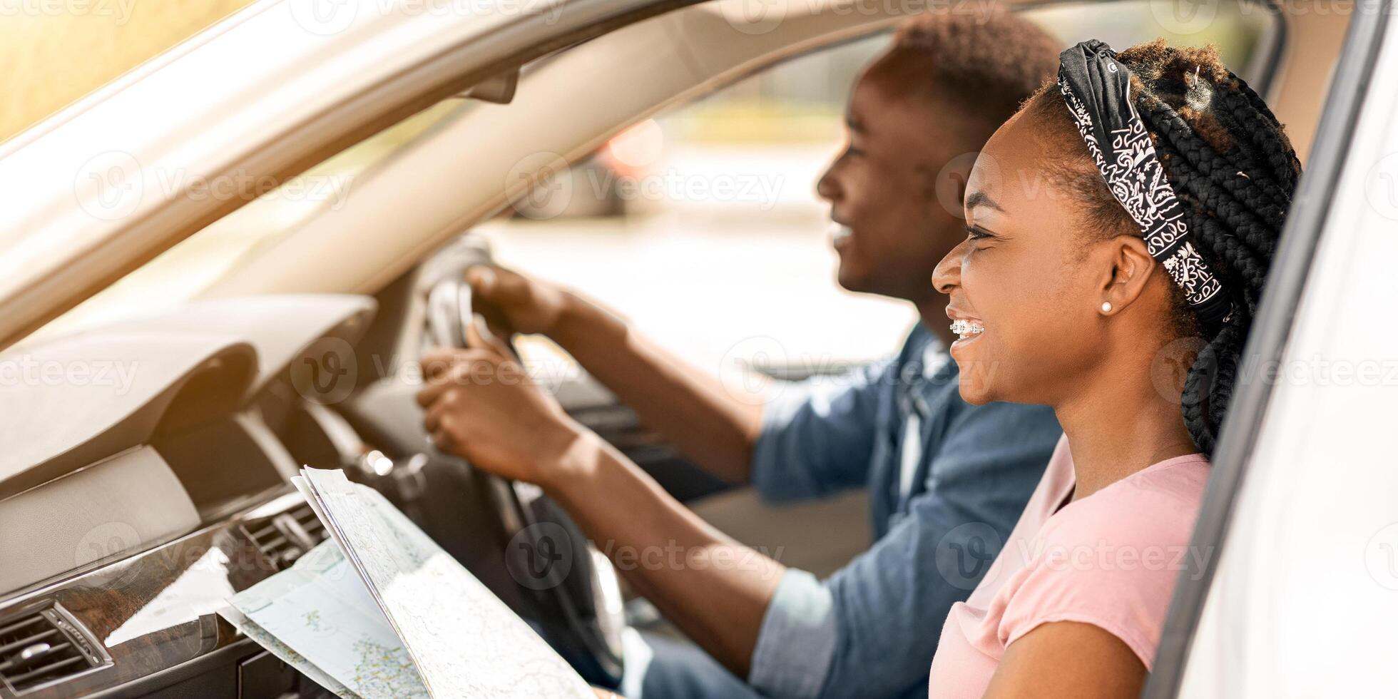 Adventurous afro american millennial couple traveling together by car, using map, looking at road and smiling, checking signs on road. Happy black man and woman having summer trip, riding auto photo